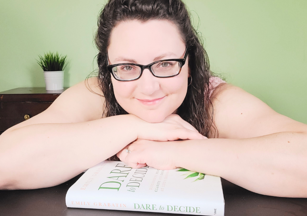 Author Emily Grabatin smiling at camera next to Dare to Decide book