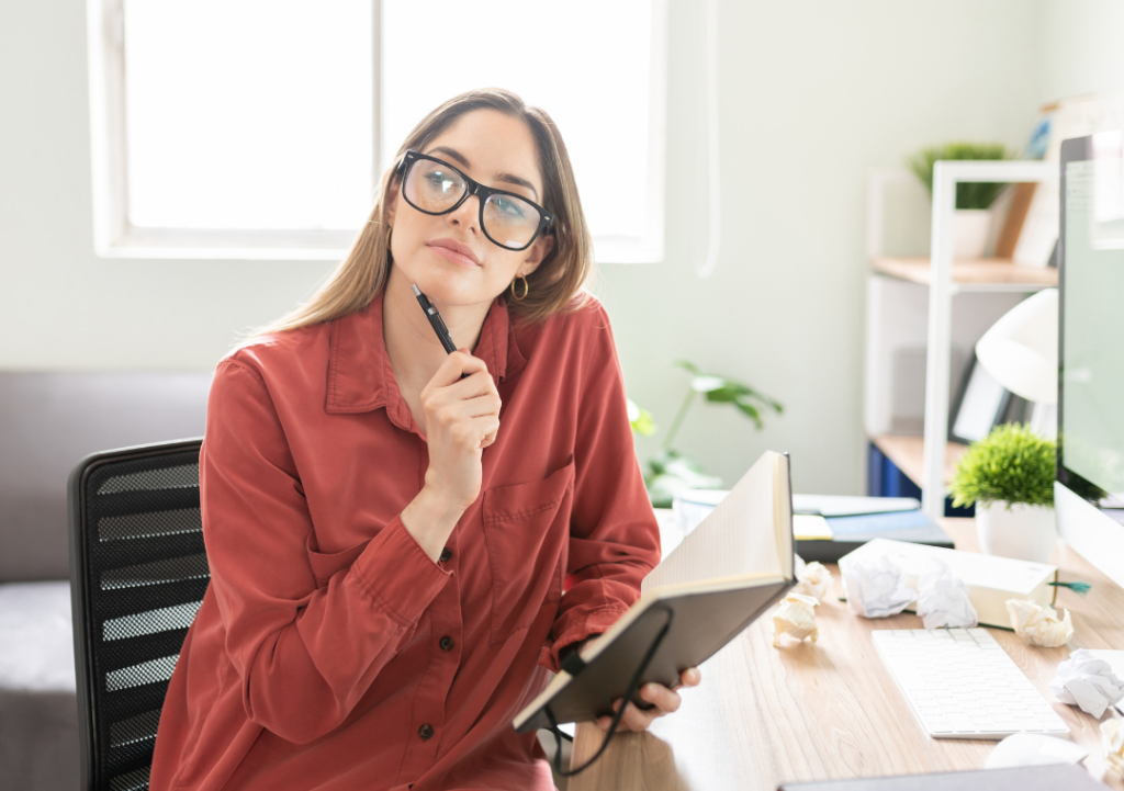 woman with glasses at desk pondering to traditional publish or self publish