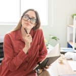 woman with glasses at desk pondering to traditional publish or self publish